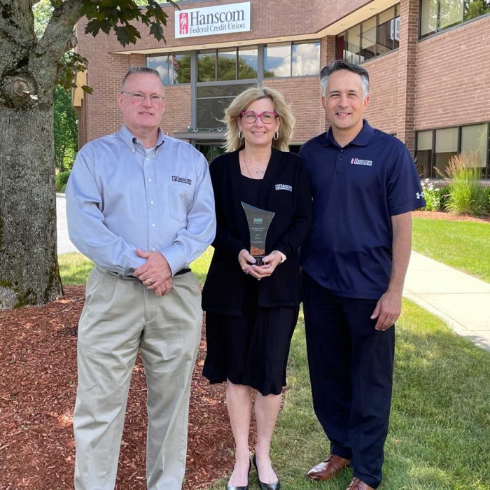 3 people stand in front of Hanscom FCUs Littleton office holding an award