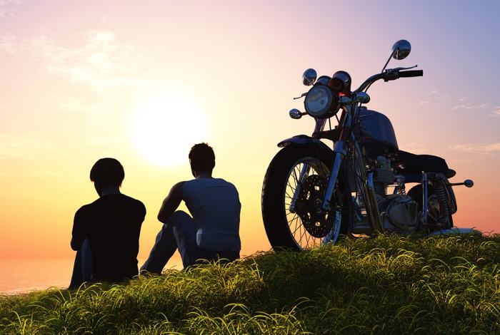 silhouette of couple sitting lakeside next to their motorcycle at sunset