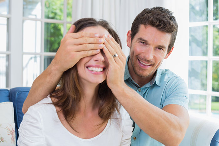 Man smiling covering woman's eyes with his hands