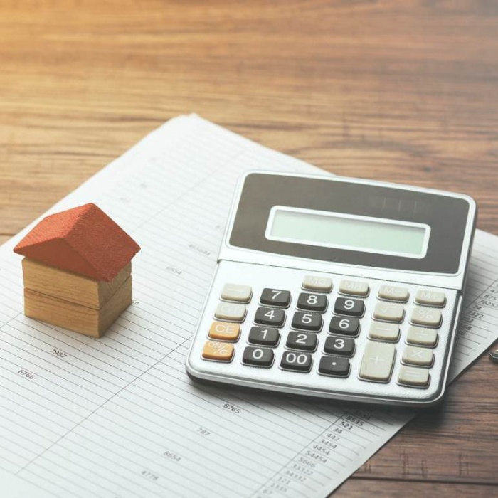 calculator on top of paper spreadsheet next to small wood house model