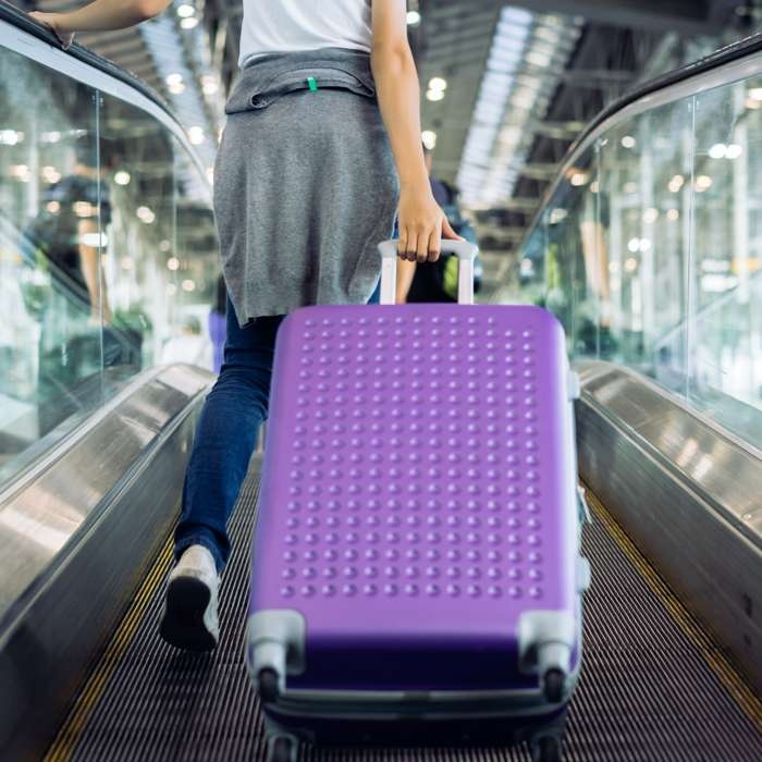 young woman pulling purple luggage on moving walking in airport